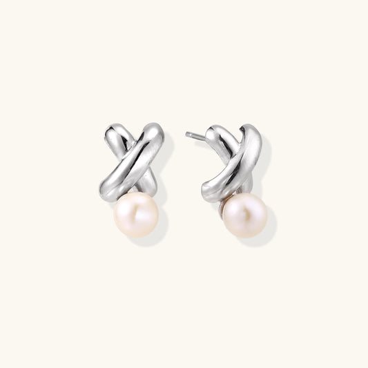 Rhodium-plated silver earrings with twisted X design and freshwater pearl drops on beige background