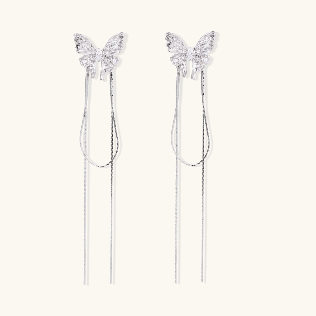 Pair of silver threader earrings with crystal butterfly tops and long chain drops on cream background.