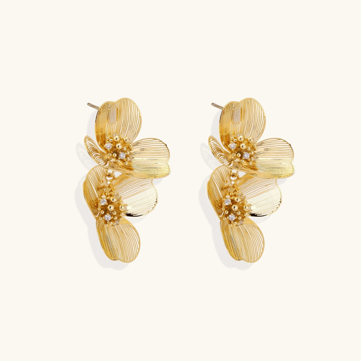 Pair of gold-plated double flower earrings with textured petals and crystal centers on cream background.