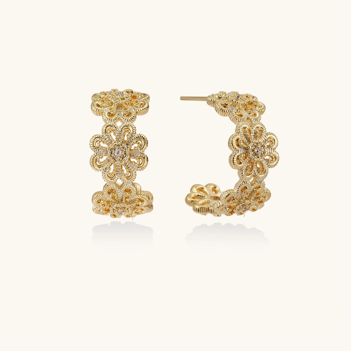 Gold hoop earrings with intricate three-dimensional floral filigree pattern in 14K gold plated brass on cream background