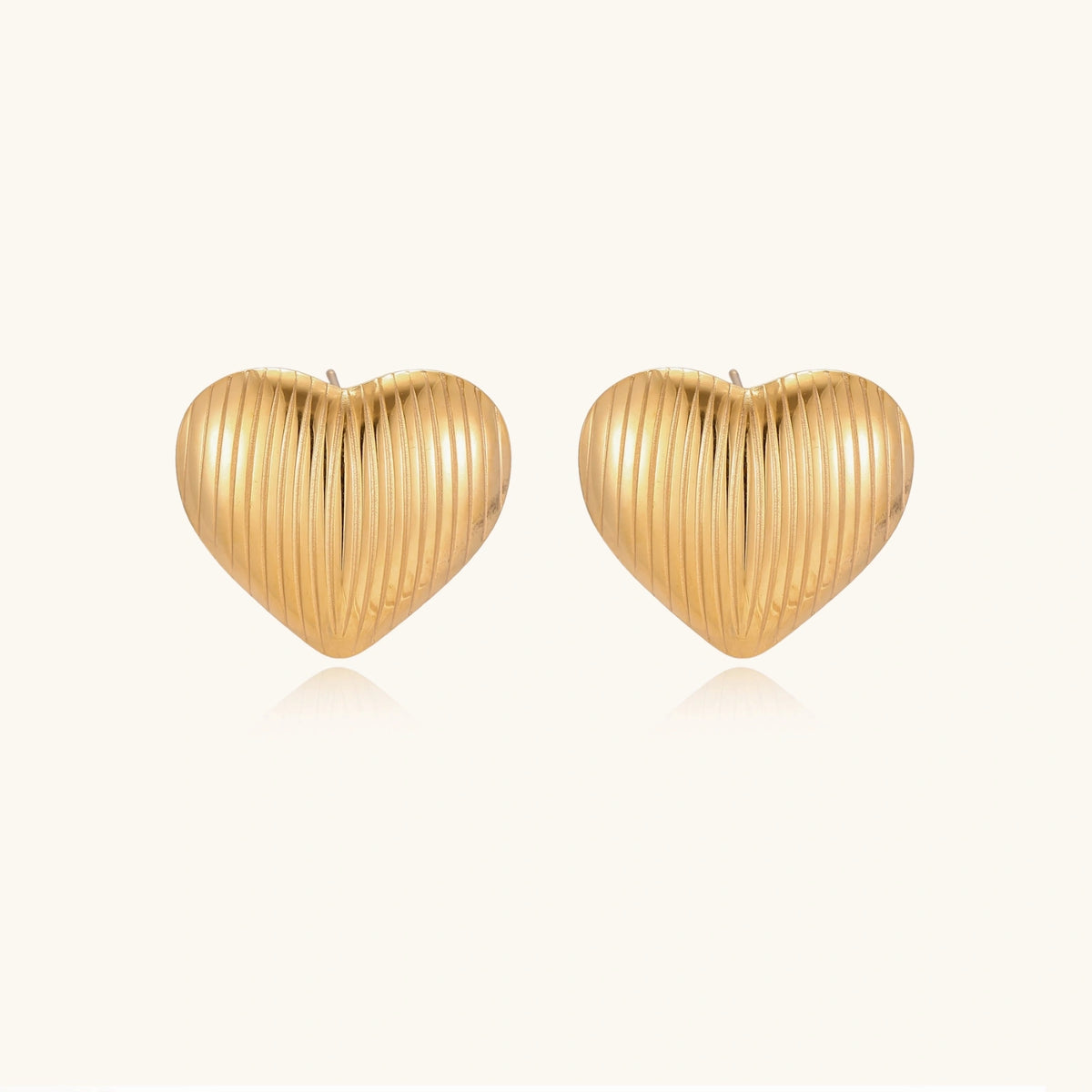 Gold heart-shaped stud earrings with parallel ridged texture on cream background