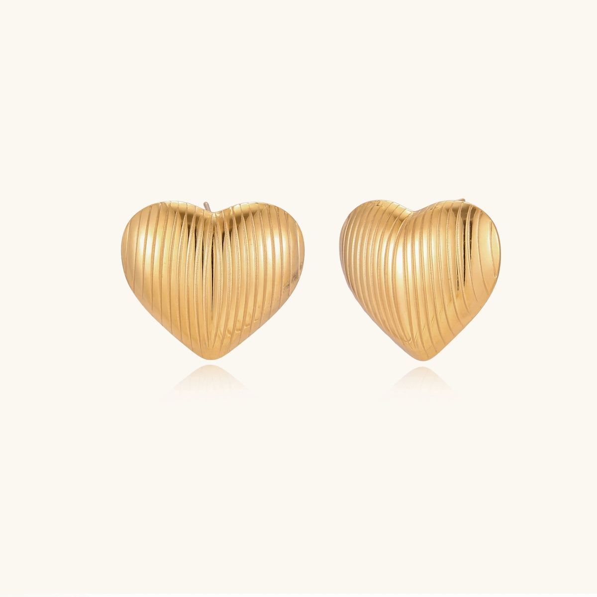 Gold heart-shaped stud earrings with parallel ridged texture on cream background